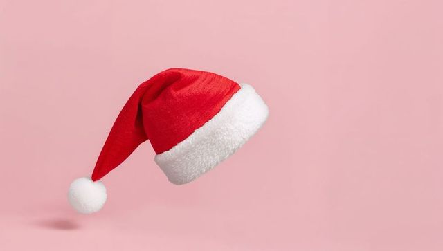 Tilting Santa Hat on Pink Background with White Fur Trim and Pompom for Holiday Design