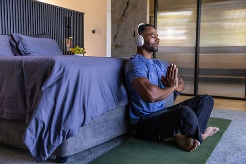 African man meditating in bedroom wearing headphones practicing mindfulness and yoga