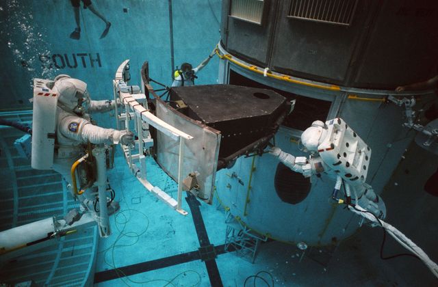 Astronauts practicing with training versions of Extravehicular Mobility Units in underwater environment at Johnson Space Center. They are rehearsing the repair mission for the Hubble Space Telescope. Useful for educational materials about space missions, NASA training programs, or space exploration.