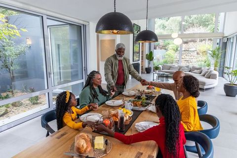 Multigenerational african american family holding hands at dining table in sunlit modern home
