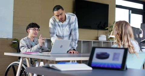 Inclusive team collaborating around laptop with wheelchair user leading office meeting
