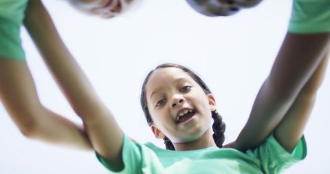 Girls huddling and cheering under bright sun with braided leader in green shirts