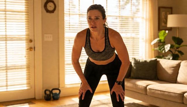 Woman pausing after kettlebell set in sunlit living room workout, catching breath