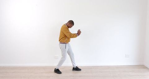 Man Dancing Energetically in Casual Attire Against White Wall