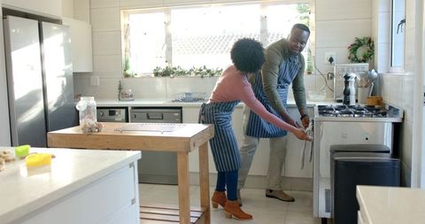 Couple cooking together in bright modern kitchen opening oven wearing striped aprons