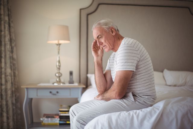 Tensed man sitting on bed in bedroom at home