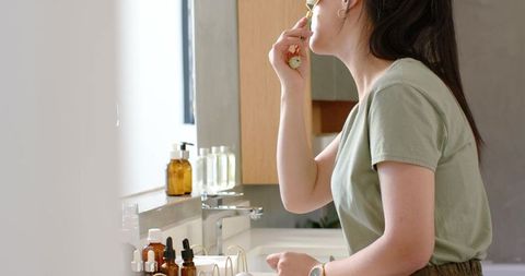 Asian woman using facial roller at bathroom vanity for modern glowing skincare routine