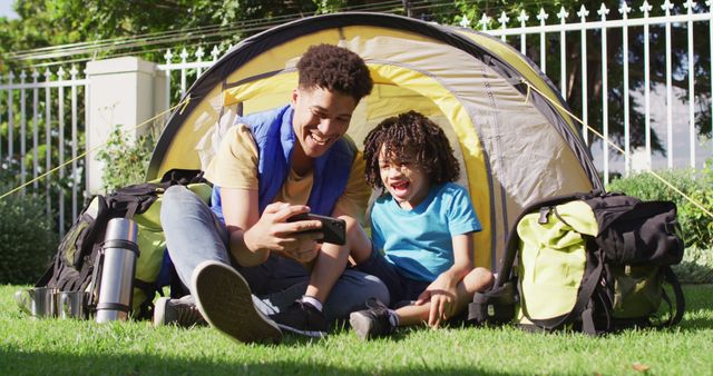 Happy biracial man and his son using smartphone in garden. domestic life, spending time at home.