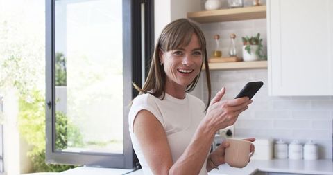 Woman Enjoying Coffee With Smartphone in Bright Kitchen