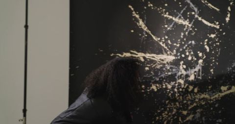 African american woman examining black canvas with beige splatter art in modern gallery