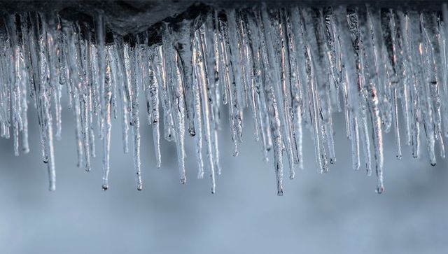 Glinting icicles hanging from roof eave with dripping water, frost detail and sunrise reflection