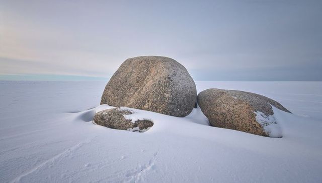 Resting granite boulders on snow-covered plain at low horizon, minimalist winter landscape