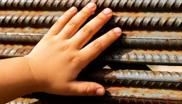 Child touching rusty ribbed rebar with bare hand showing texture and contrast