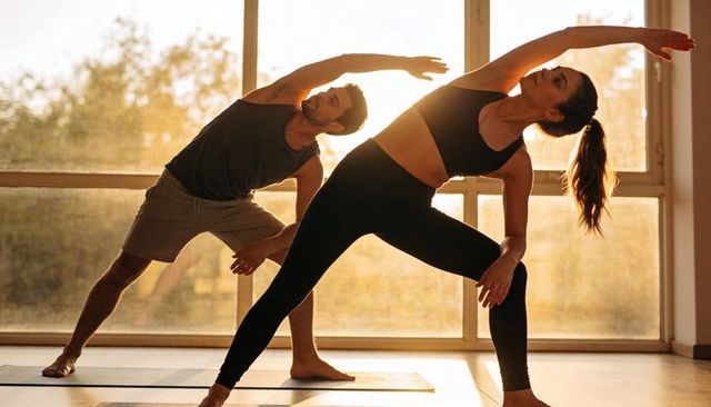 Couple practicing yoga side-bend in sunlit studio for flexibility, fitness, wellness