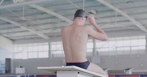 Competitive swimmer adjusting goggles at poolside with lane ropes
