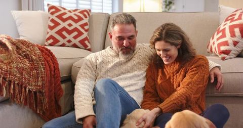 Couple relaxing on living room floor petting dog in cozy cable knit sweaters