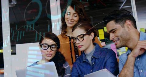 Collaborating coworkers leaning over laptops and tablet in office with data overlays