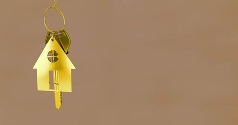 Golden house keychain hanging from ring with key and hexagonal fob on brown background