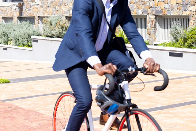 Midsection of african american businessman in suit riding a bike. Business, work, corporation, recreation and healthy lifestyle concept.