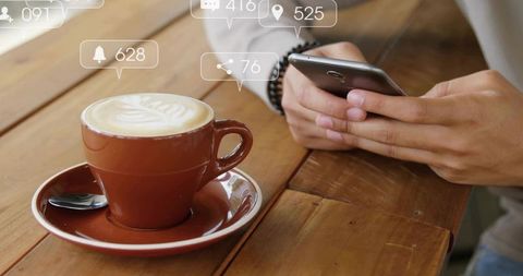 Browsing Smartphone Beside Latte Art Cup on Wooden Table with Social Media Notifications