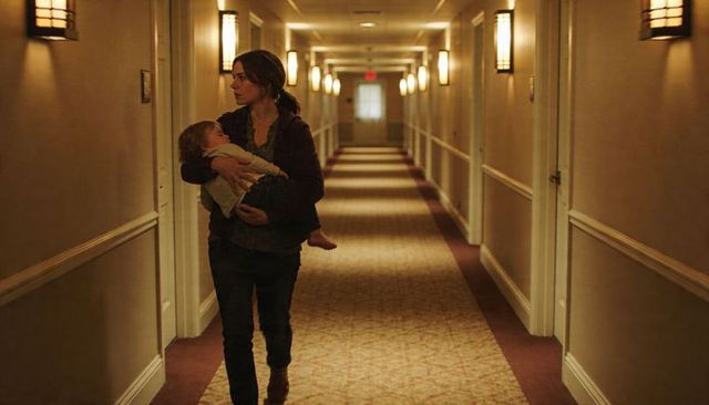 Mother carrying sleeping child through dimly lit hotel corridor, quiet nighttime care