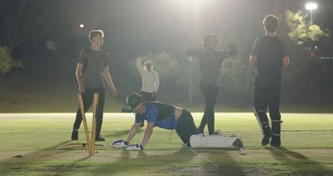 Night cricket celebrating wicket under floodlights, fielders appealing and umpire raising finger