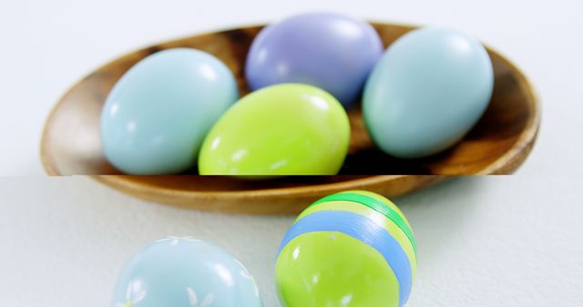 Colorful Easter eggs are arranged in a wooden bowl and on a white surface, with copy space. Their pastel colors and the egg theme suggest a festive celebration of Easter.