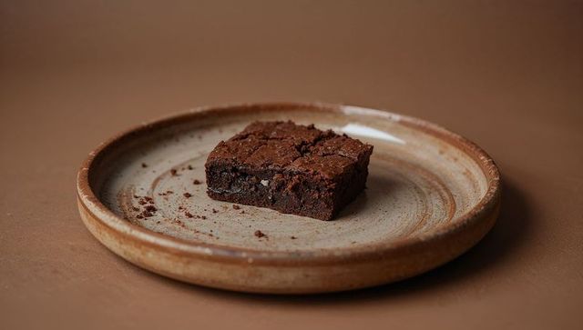 Fudgy chocolate brownie sitting on rustic ceramic plate with crumbs