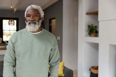 Thoughtful african american senior standing in modern living room wearing sage crewneck