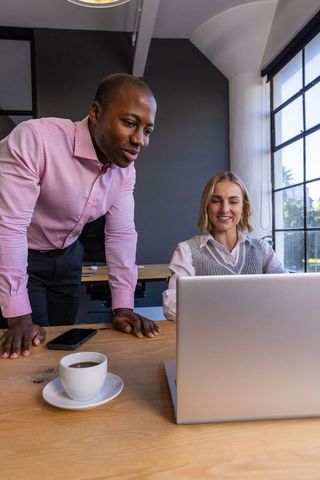 Diverse coworkers collaborating on laptop project in modern office