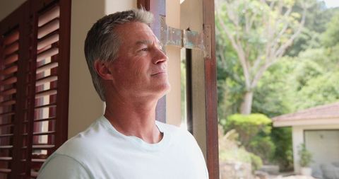 Mature Man Enjoying Sunny Garden View from Cozy Home
