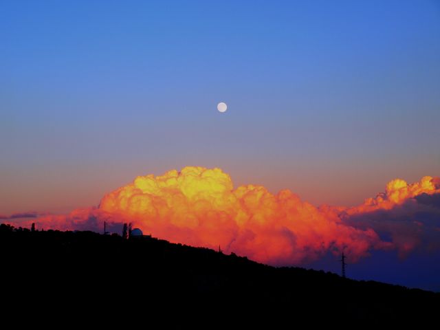 Capturing a stunning sunset with a full moon against a backdrop of glowing clouds. Ideal for use in travel blogs, nature magazines, or motivational posters. Highlights the beauty of nature and tranquility of twilight hours.
