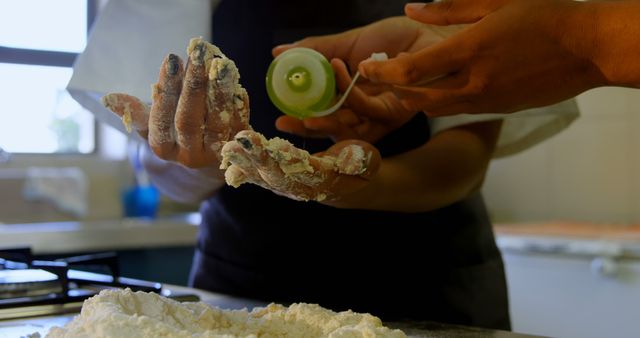 Hands busy kneading dough with flour in a sunny kitchen setting. One person is aiding another with baking utensils, showcasing teamwork and preparation. Suitable for illustrating homemade baking, culinary activities, teamwork in the kitchen, or cooking tutorials.