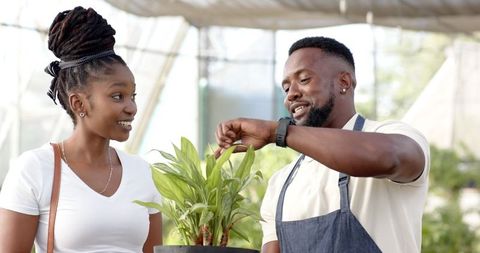 Greenhouse worker and customer examining plant indoors