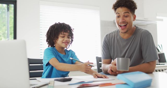 Happy biracial man and his son doing homework together. domestic life, spending time at home.