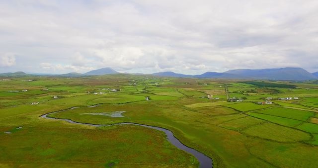 This aerial shot showcases the picturesque Irish countryside with its lush green patchwork fields and a winding river. The scenic landscape can be used in travel brochures, agricultural publications, or as a visual representation of rural serenity and natural beauty. Ideal for promoting Irish tourism or rural living images.