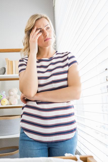 Depressed woman in deep thought standing near window at home