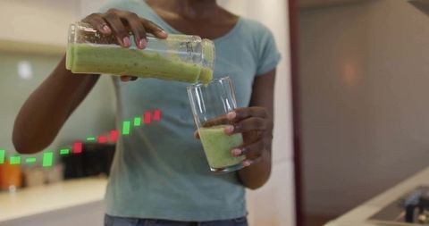 Woman pouring green smoothie into glass at kitchen counter for healthy lifestyle