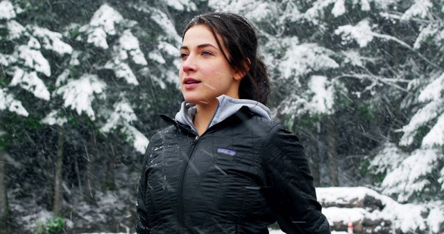 Woman wearing black jacket standing in snowy forest, appearing to enjoy the serene winter environment. Perfect for promoting winter wear, outdoor adventures, and healthy lifestyle content. Suitable for use in advertisements, blogs, and social media promoting winter activities or nature exploration.