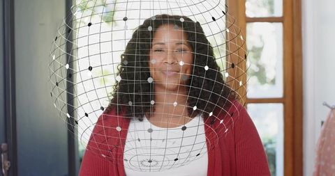 Smiling woman standing in home entryway wearing red cardigan with digital globe overlay