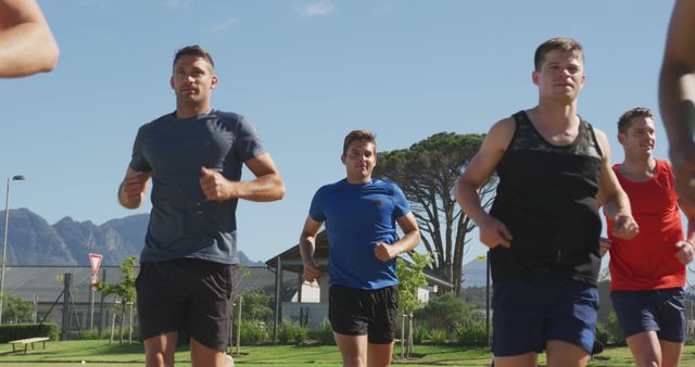 Group of young Caucasian men jogging outdoors, with copy space. They're enjoying a fitness session in a park with a scenic mountain backdrop.