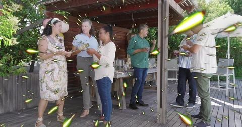 Adults chatting under pergola at backyard summer gathering with buffet and light streaks