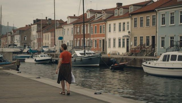 Woman walking along quaint harbor canal pastel houses boats wooden quay evening stroll
