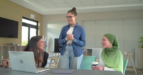 Diverse female team collaborating around laptop in bright modern office featuring hijab
