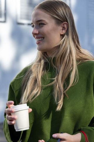 Smiling young woman holding coffee and keys while standing outdoors in green sweater