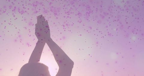 Mid-adult woman raising palms toward sun with pastel pink bokeh halo and soft glow