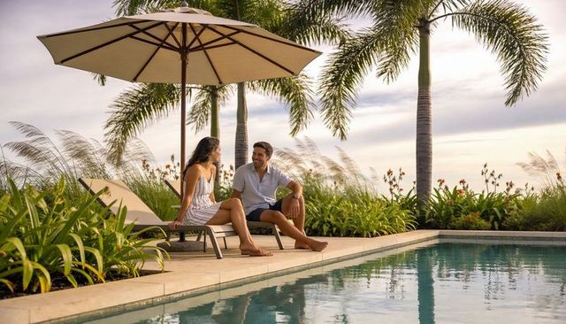 Couple relaxing and chatting poolside at tropical resort with palms and cocktail