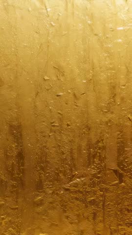 Shimmering gold panel revealing rising backlight and flowing droplets in vertical motion