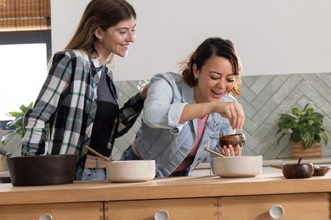 Friends sprinkling spice while cooking at kitchen island, casual home cooking moment