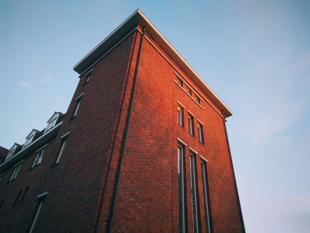 Imposing red brick building set against a clear blue sky at sunset. Highlights the architectural details of the tall structure with sunlight casting a warm glow. Ideal for urban and architectural magazines, promotional materials for real estate, historic urban development, or representing cityscapes.